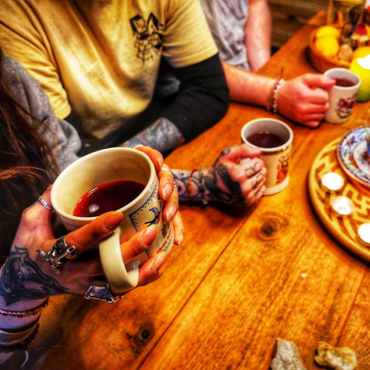 Tattooed people drinking loose leaf tea with patterned mugs and tealight candles on a wooden table